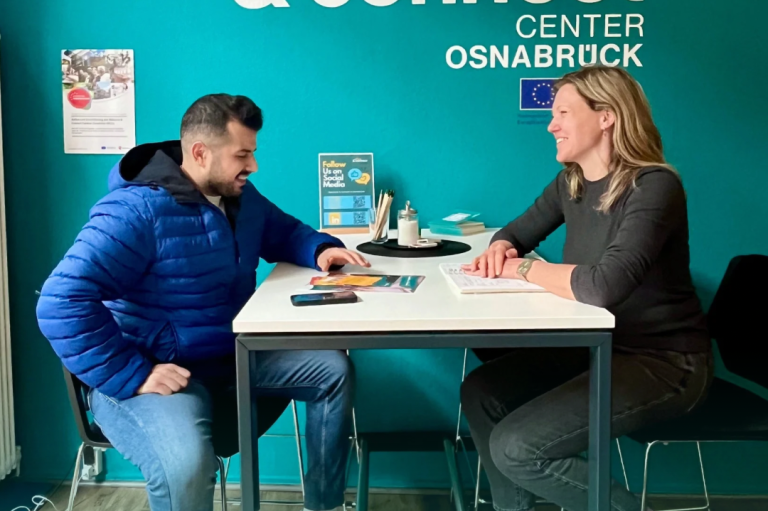 Zwei Personen sitzen auf Liegestühlen vor einem Gebäude und unterhalten sich.