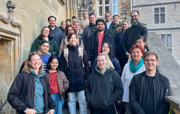 Gruppenfoto von 24 Personen auf einer Treppe vor einem historischen Gebäude.