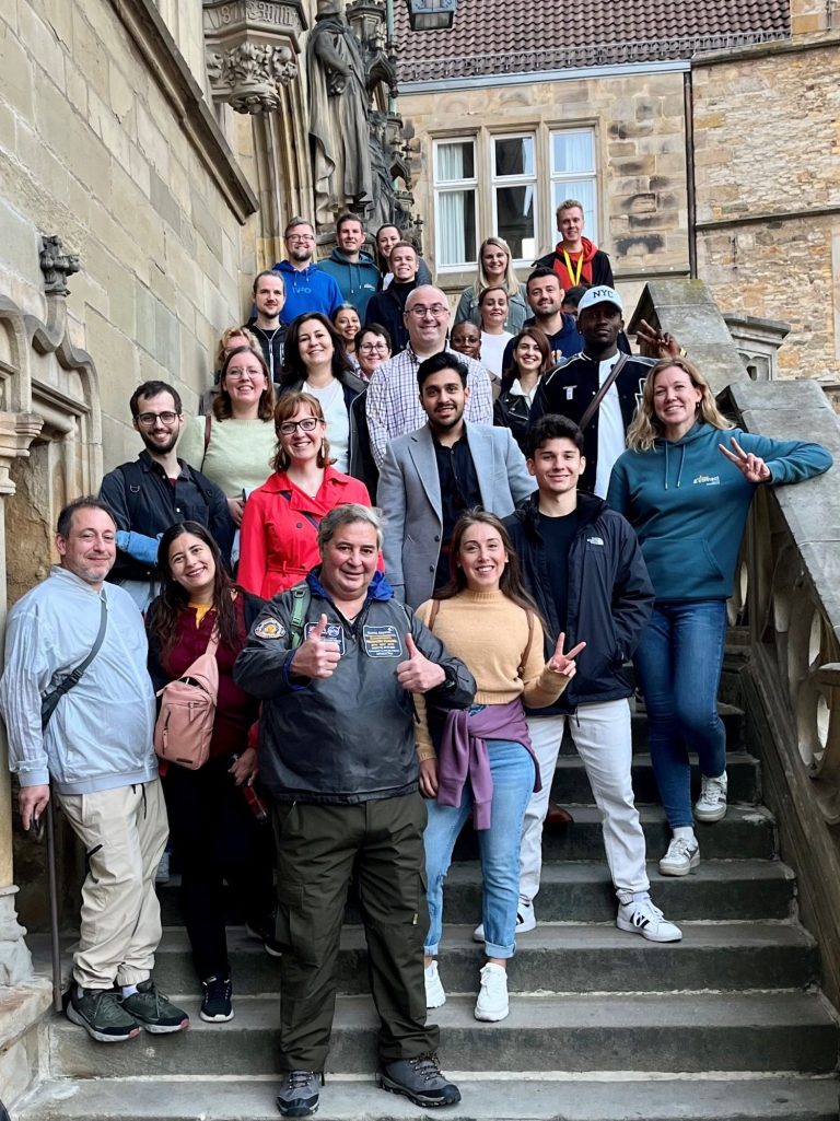 Gruppensfoto von 15 Personen, die auf einer Treppe vor einem historischen Gebäude stehen.